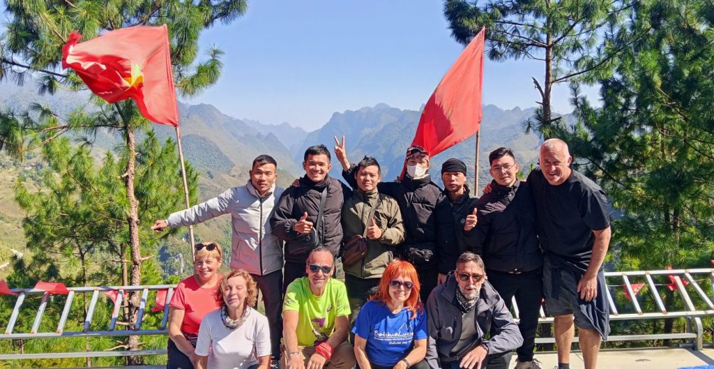 Grupo de viajeros sonriendo en un mirador de Vietnam con banderas y montañas al fondo