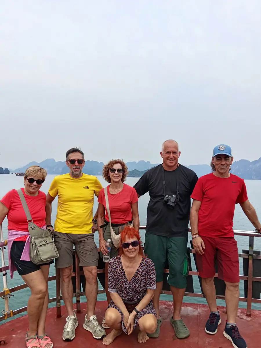 Viajeros posando juntos en la cubierta de un barco con formaciones rocosas al fondo en Vietnam